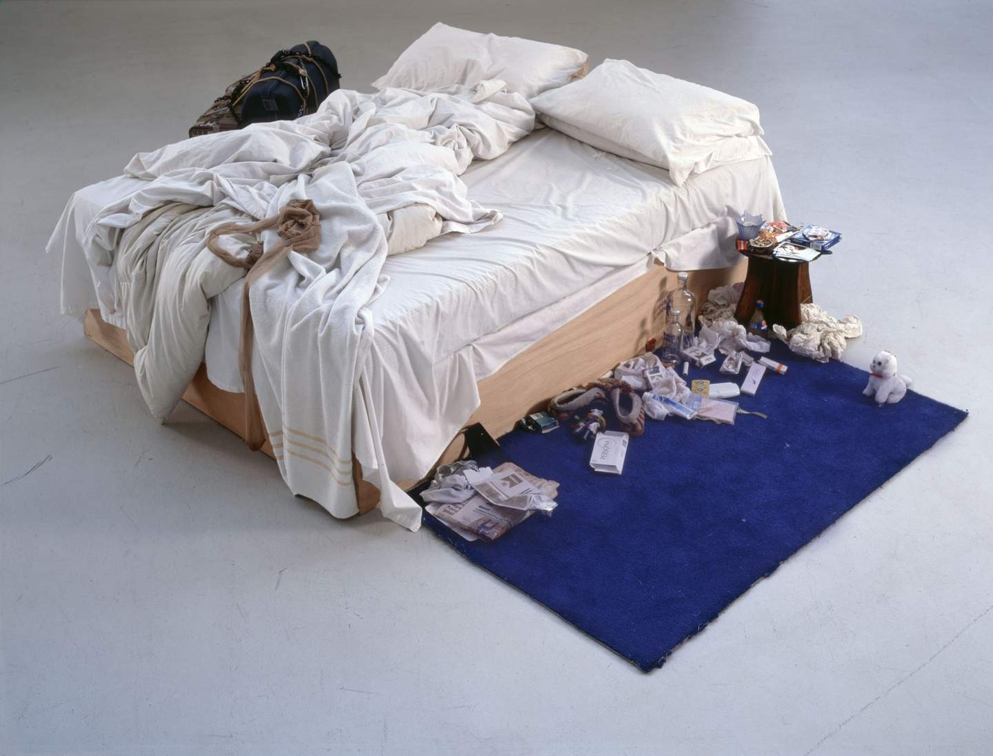 Instalacja Tracey Emin "My bed" – łóżko ze zmiętą pościelą ustawione w białej, galeryjnej przestrzeni. Wokół porozrzucane przedmioty osobiste, notatki, kosmetyki, leki.