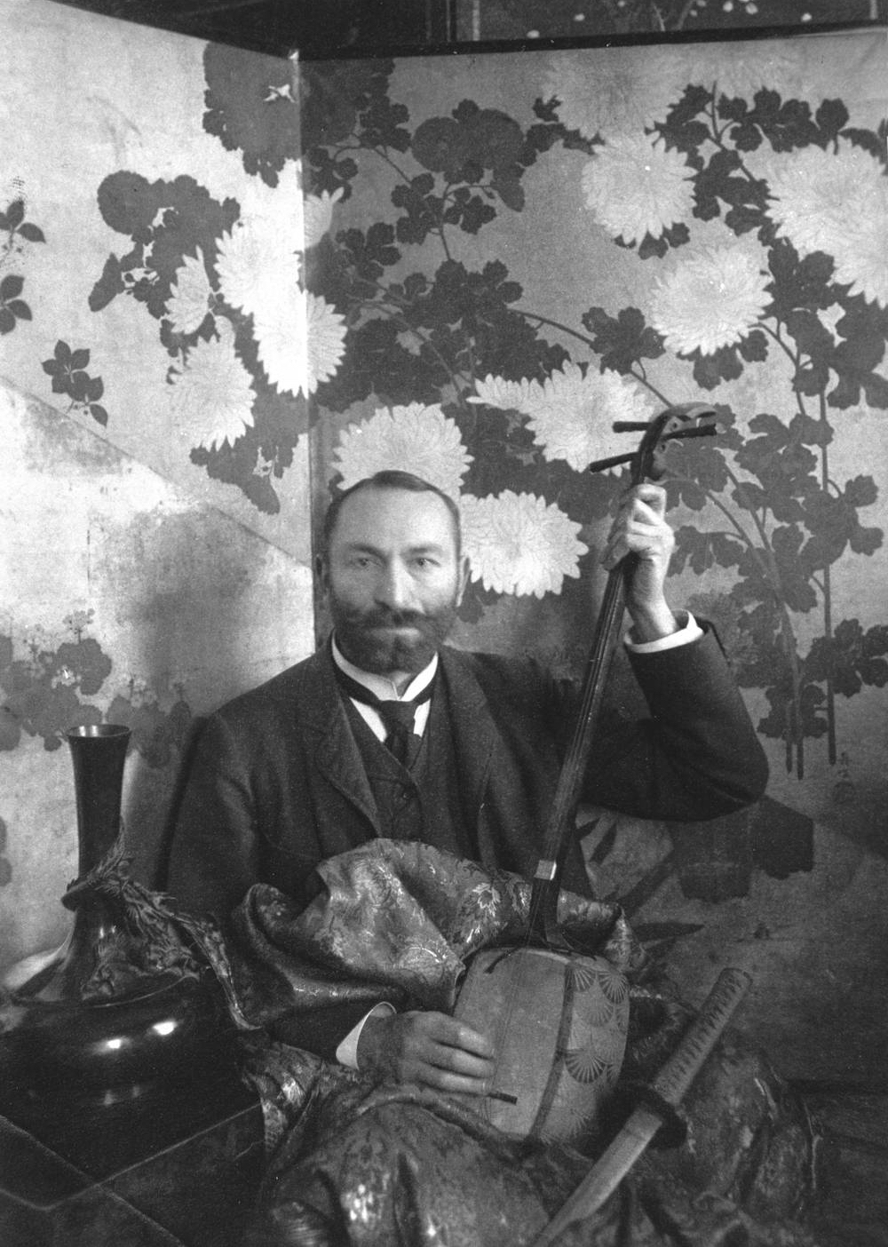 Feliks „Manggha” Jasieński, czarno biały portret mężczyzny w garniturze, trzymającego tradycyjny japoński instrument strunowy